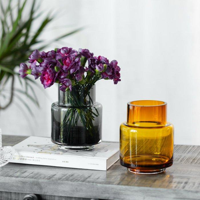 Lila Nelken in schwarzem Glasvase auf Holztisch, daneben orangefarbene Vase – perfekt für Blumensträuße & Geschenke