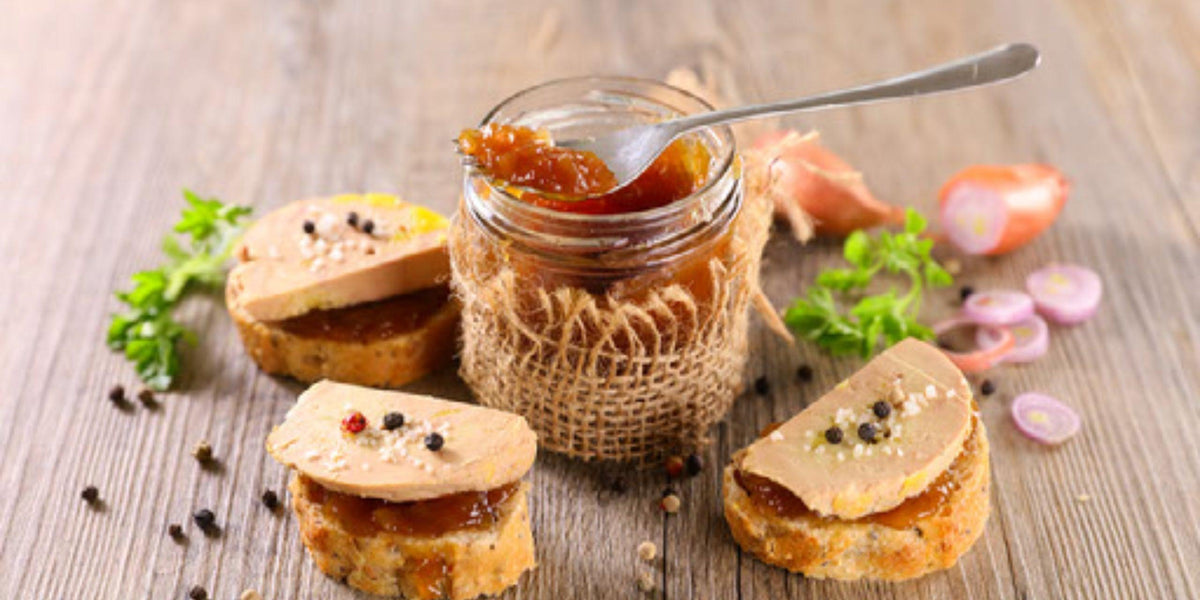 Feine Foie Gras-Canapés mit hausgemachter Marmelade und frischen Kräutern auf Holztisch