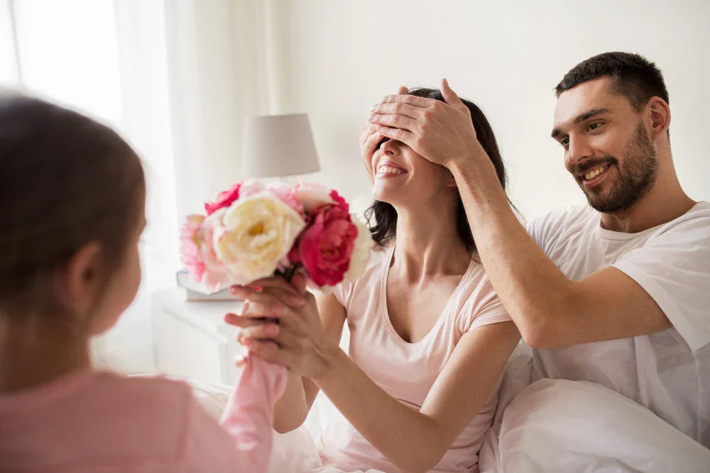 Familie überrascht Mutter mit Blumenstrauß im Bett – frische Rosen für besondere Momente