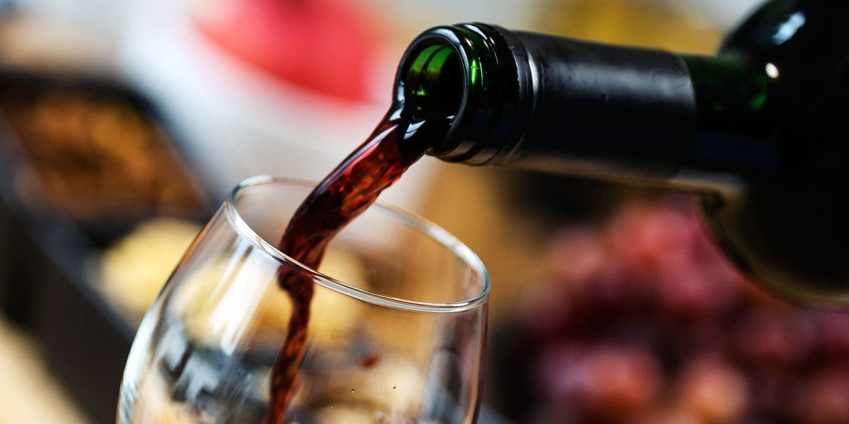 Rotwein wird aus Flasche in Glas gegossen – perfekt zu Geschenken & Blumensträußen